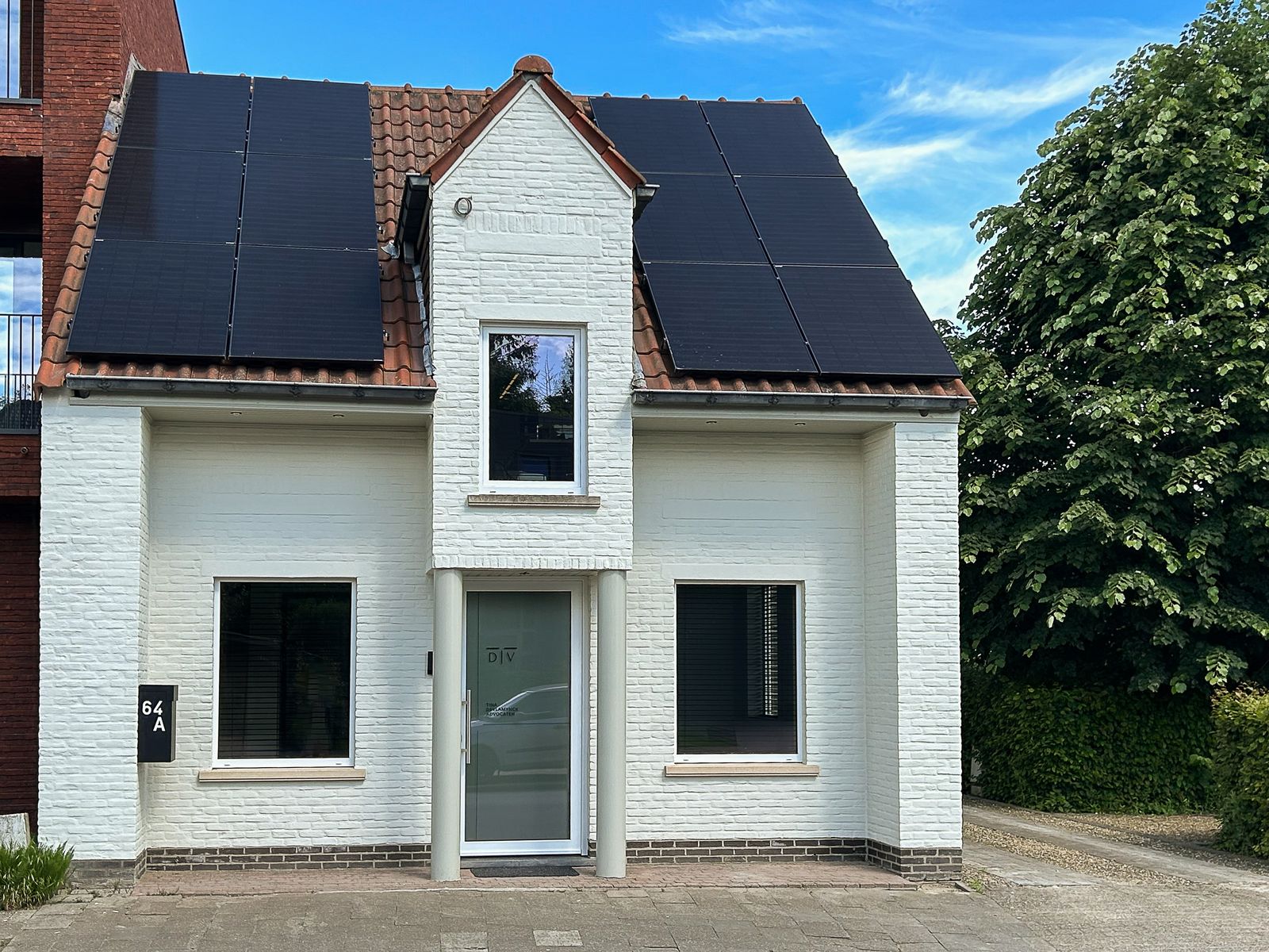 De buitenkant van het advocatenkantoor, een modern gebouw met wit geschilderde bakstenen en zonnepanelen op het dak.